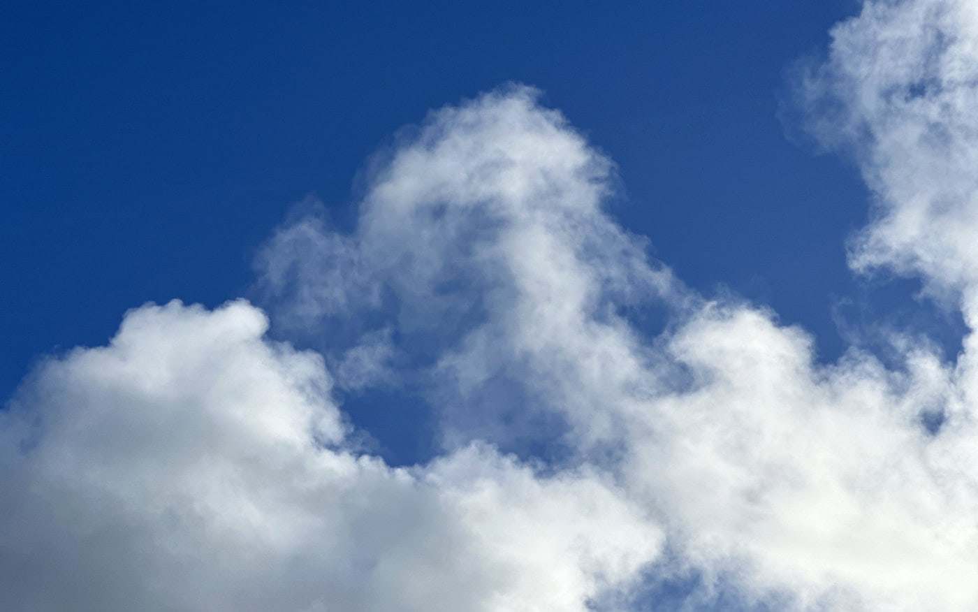 a deep blue sky seen between two patches of thin, puffy white clouds