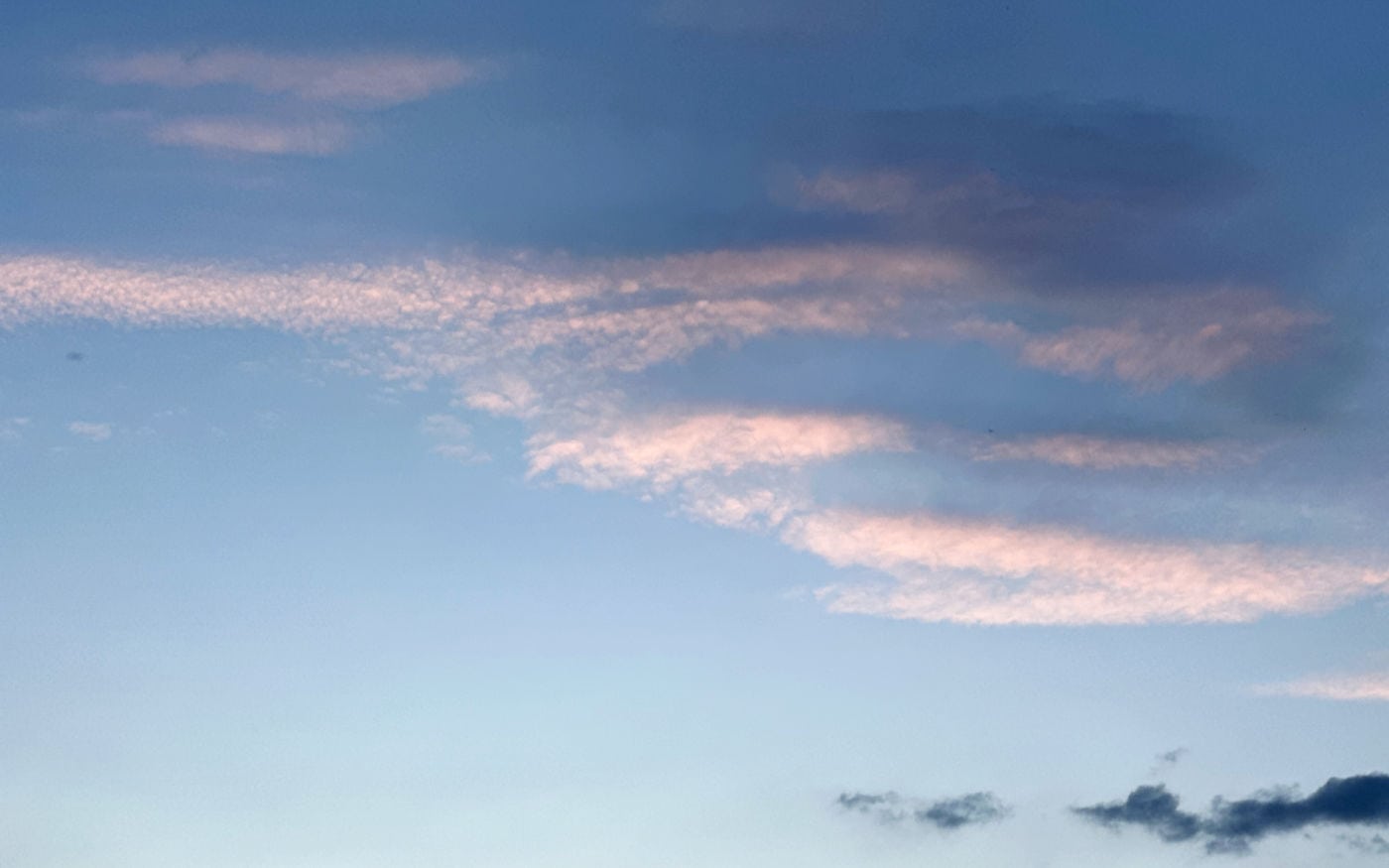 a deep blue sky seen between two patches of thin, puffy white clouds